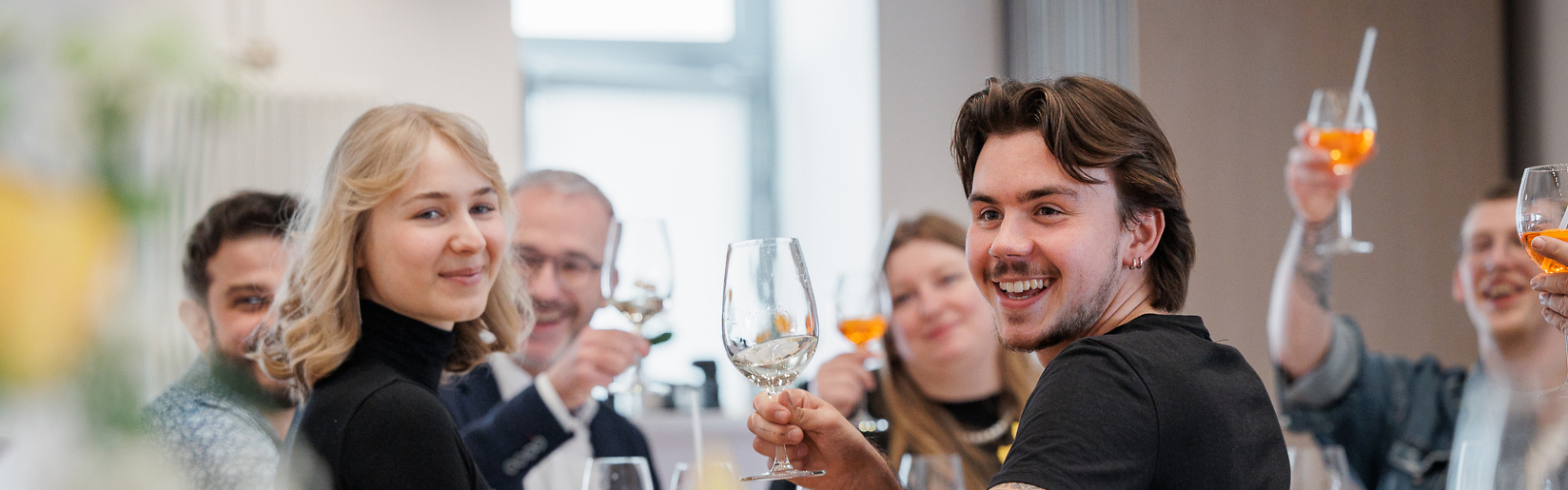 Mehrere Personen sitzen gemeinsam an einem Tisch, stoßen mit Getränken an und lachen in einem Restaurant.