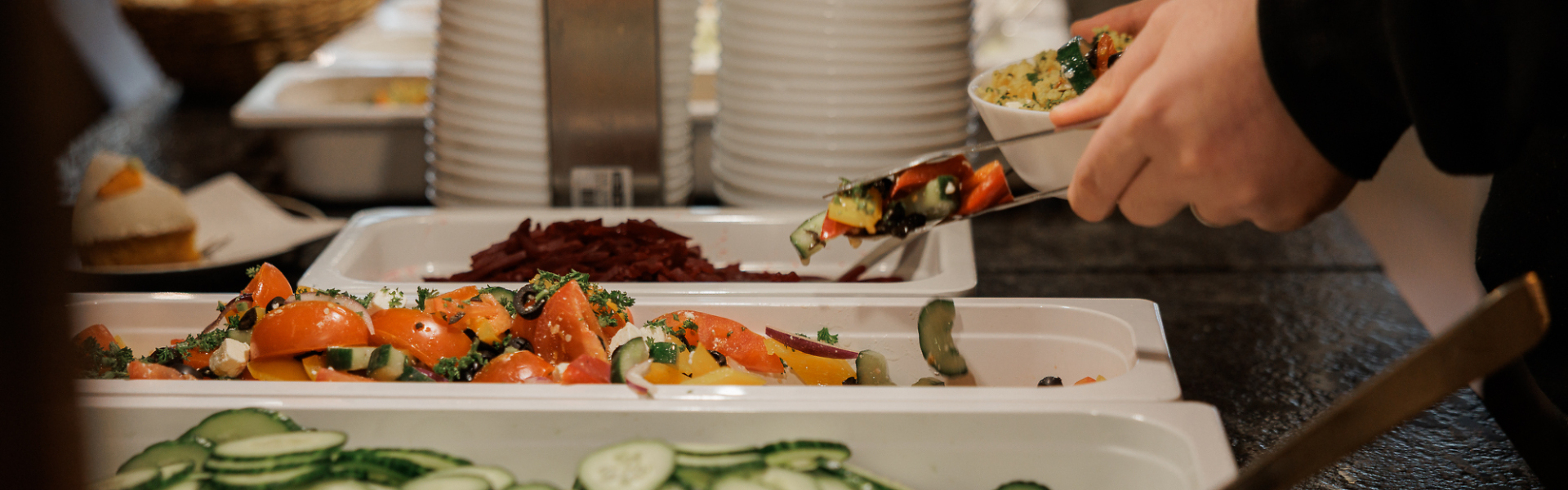Person bedient sich an einem Buffet mit verschiedenen Salaten und Beilagen und legt Speisen auf einen Teller.