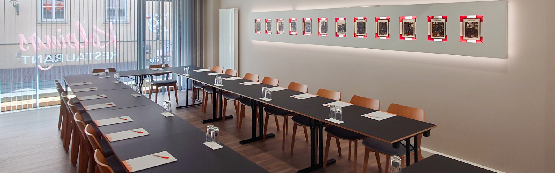 Seminarraum mit U-förmig angeordneten Tischen, ausgestattet mit Notizblöcken, Stiften und Gläsern, große Fensterfront im Hintergrund.