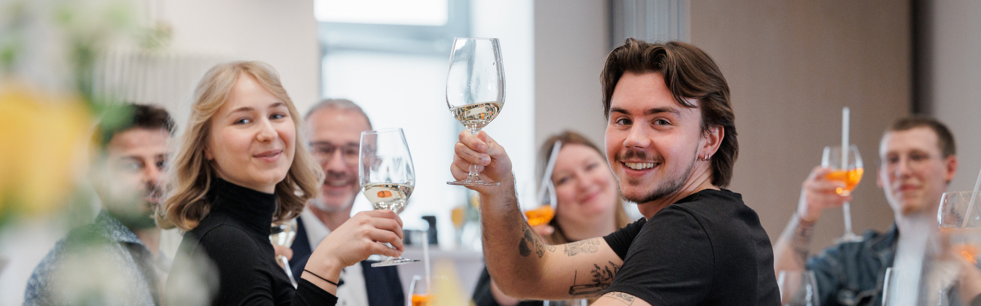 Mehrere Personen sitzen gemeinsam an einem Tisch, stoßen mit Getränken an und lachen in einem Restaurant.