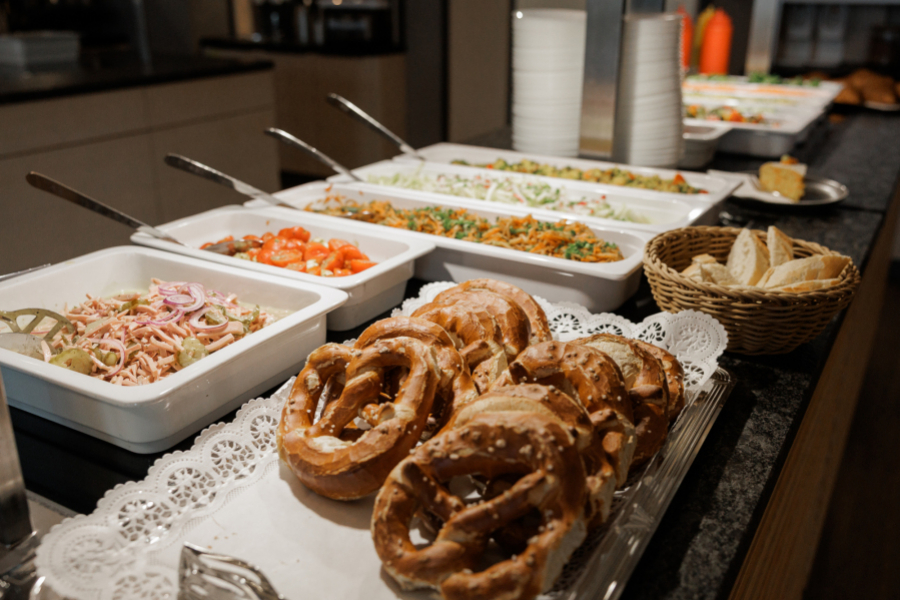 Buffet mit verschiedenen Salaten und Brezen auf einer Servierplatte sowie Brotkorb auf einer Theke angerichtet