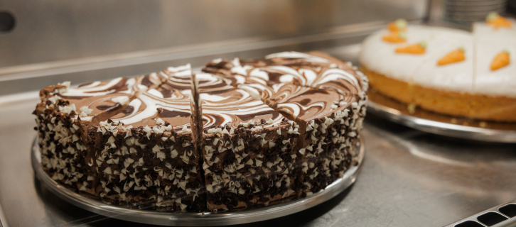 Kuchenbuffet mit angeschnittener Schokoladentorte und weiterer Torte im Hintergrund.