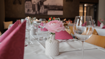 Detailaufnahme eines gedeckten Tisches mit Weinglas, rosa Serviette und Blumenvase.