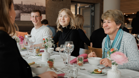 Gäste sitzen gemeinsam am Tisch, unterhalten sich und essen.