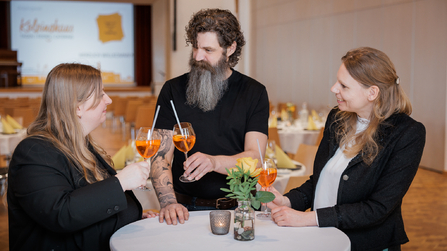 Drei Personen stoßen bei einem Stehempfang mit Aperitifs an.