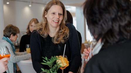 Eine Frau unterhält sich lächelnd mit einer anderen Person an einem Tisch im Restaurant.